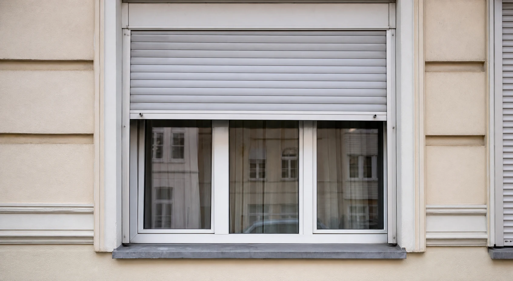 Wohnhausfenster mit halb geschlossenem Rolladen in Wien Hernals, sichtbare Fuehrungsschienen und sauberer Fensterbereich ohne Logos